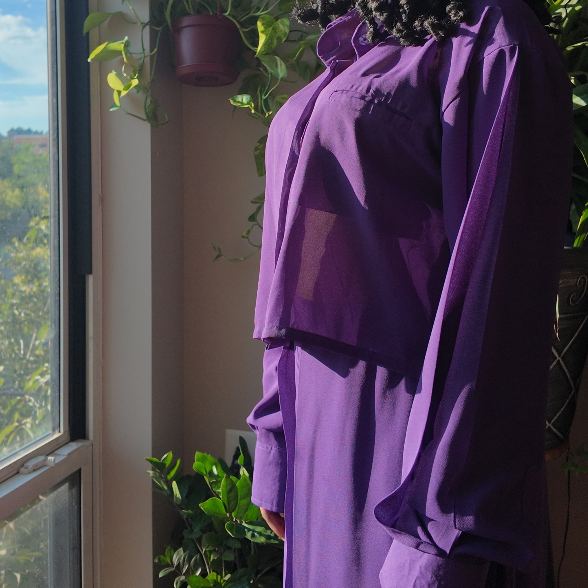 Another view of the Versatile Translucent Blouse in purple, beautifully showcasing its sheer design in a sunlit setting. This blouse is a trendy option within women's African clothing, appealing to those who love unique African apparel from esteemed African clothing brands.